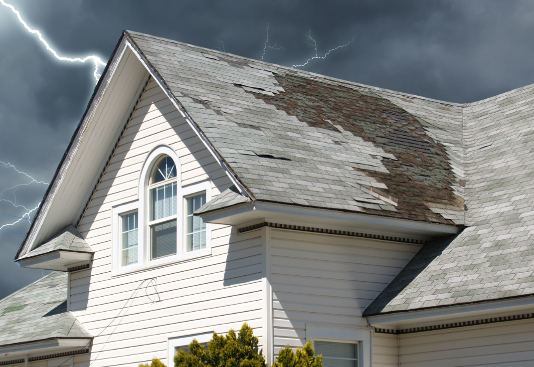 House with damaged, missing shingles on the roof under dark storm clouds and lightning